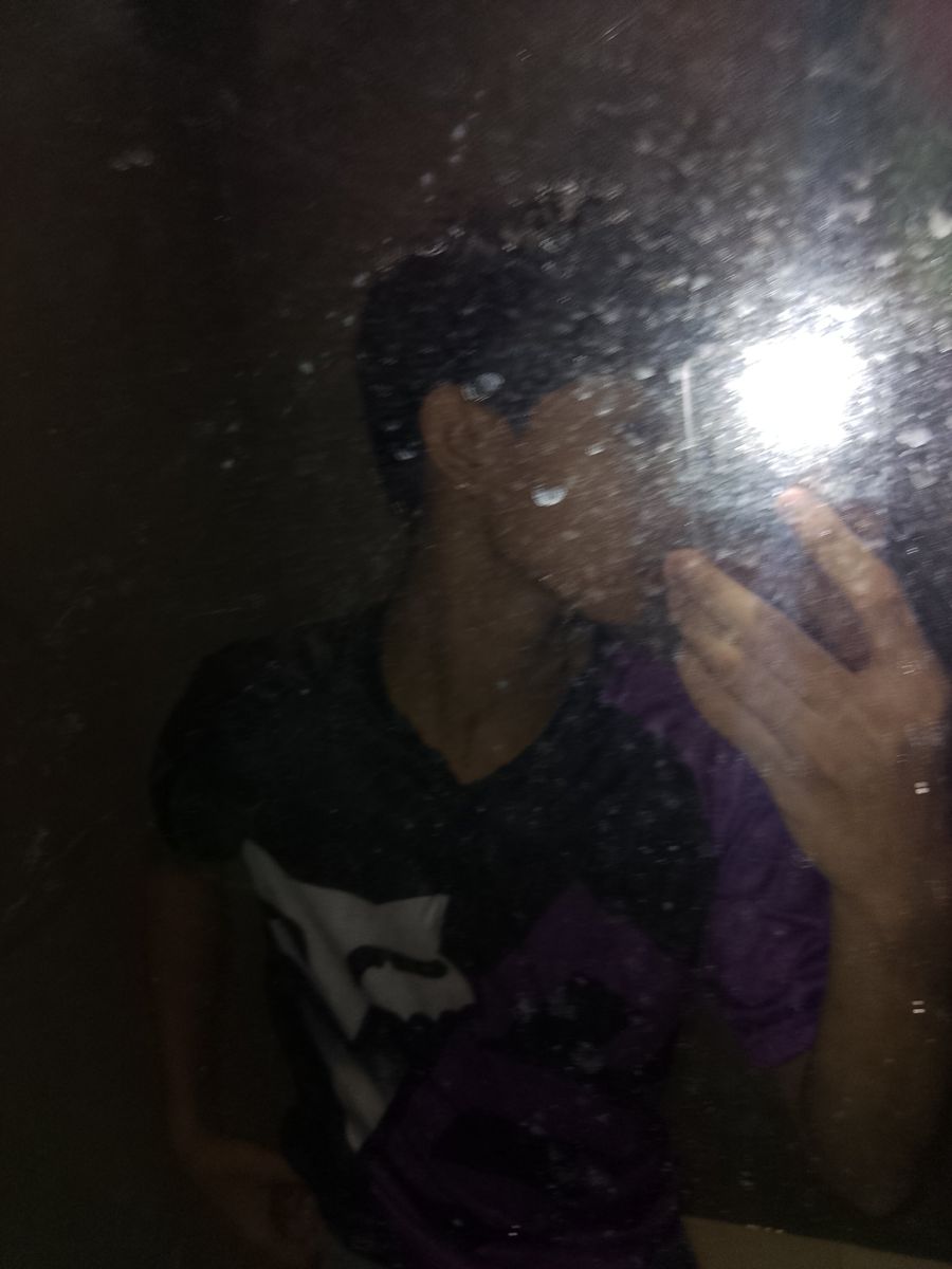 Dim mirror selfie, face covered by a hand, wearing a black graphic tee